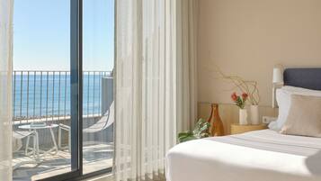 A hotel room with a balcony, a bed, a bedside table with a lamp, and a view of the sea.