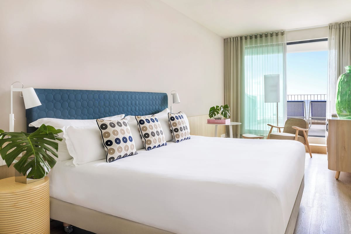 Ein Hotelzimmer mit einem großen Bett, zwei Nachttischlampen, einem Topf mit einer Pflanze, einem kleinen Tisch und einem Stuhl.