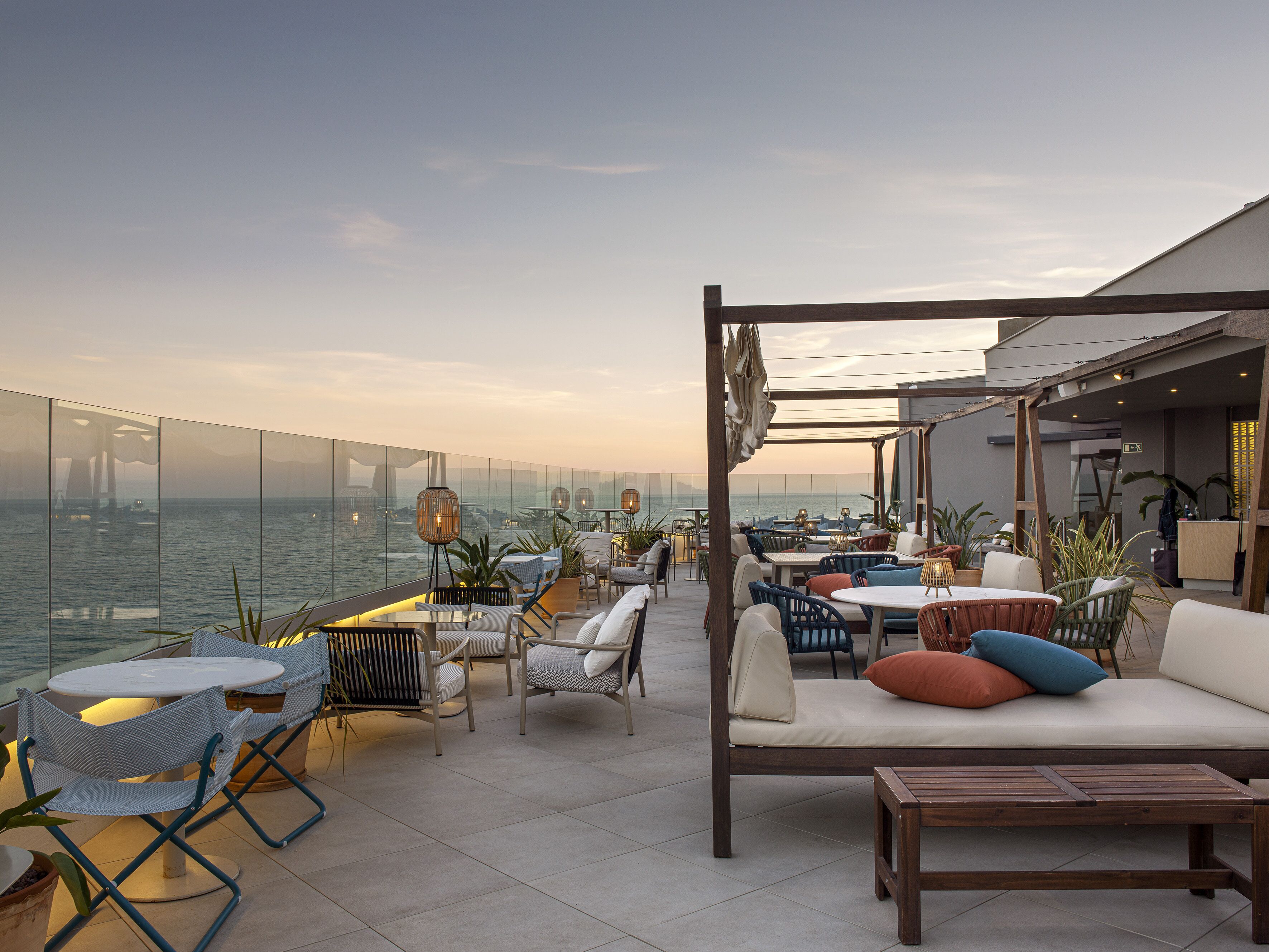 Una terraza en la azotea con mobiliario exterior, vistas al mar y una barandilla de cristal.
