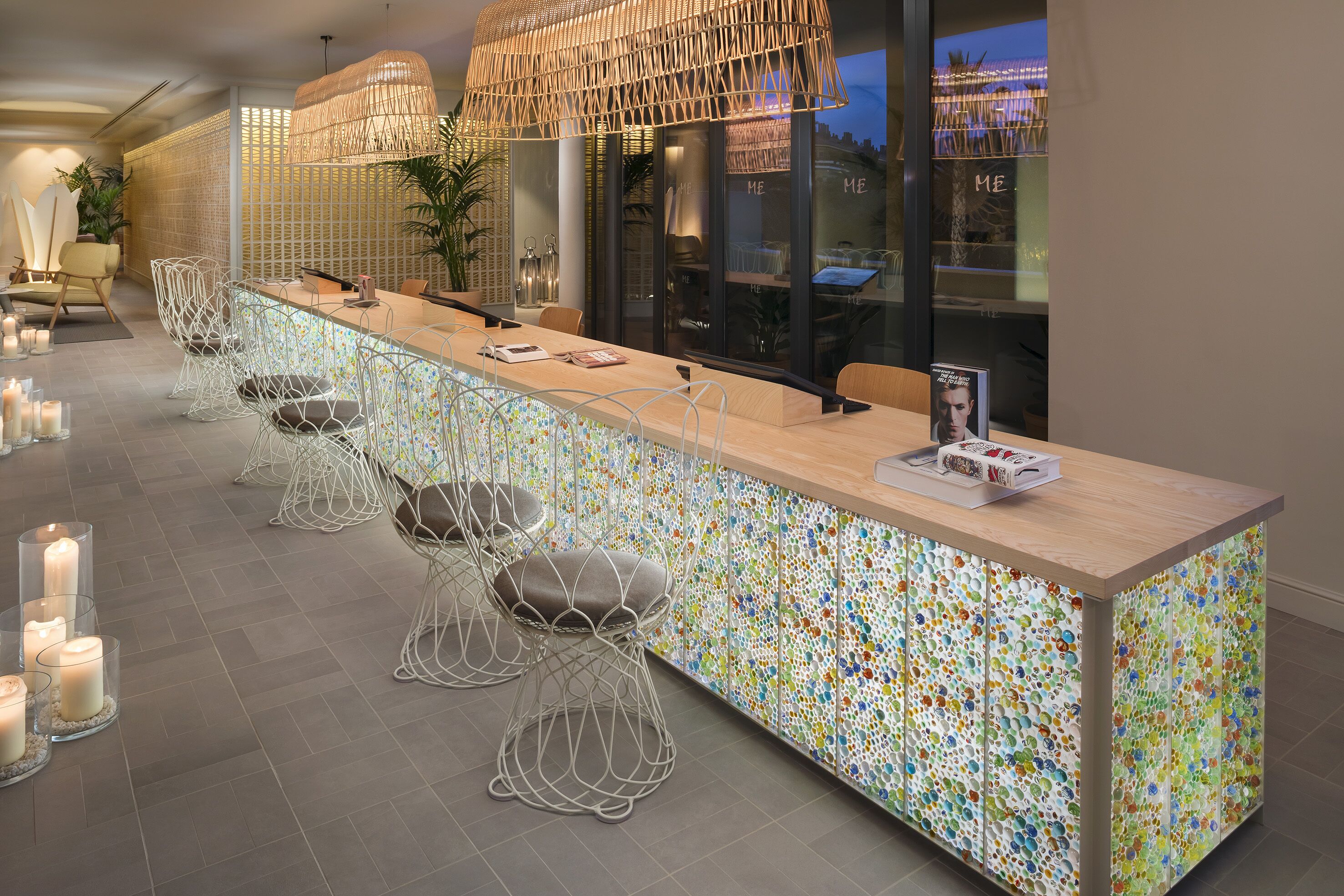 Un área de bar moderna con una barra larga, sillas de estructura metálica y velas en el suelo.