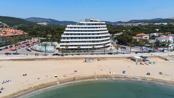 Un hotel de varios pisos con un patio central, rodeado por una playa y montañas.