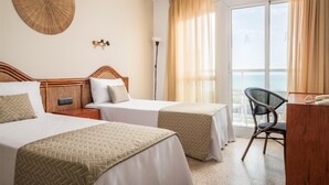 Habitación de hotel con dos camas, un escritorio, una silla y un ventanal con cortinas.