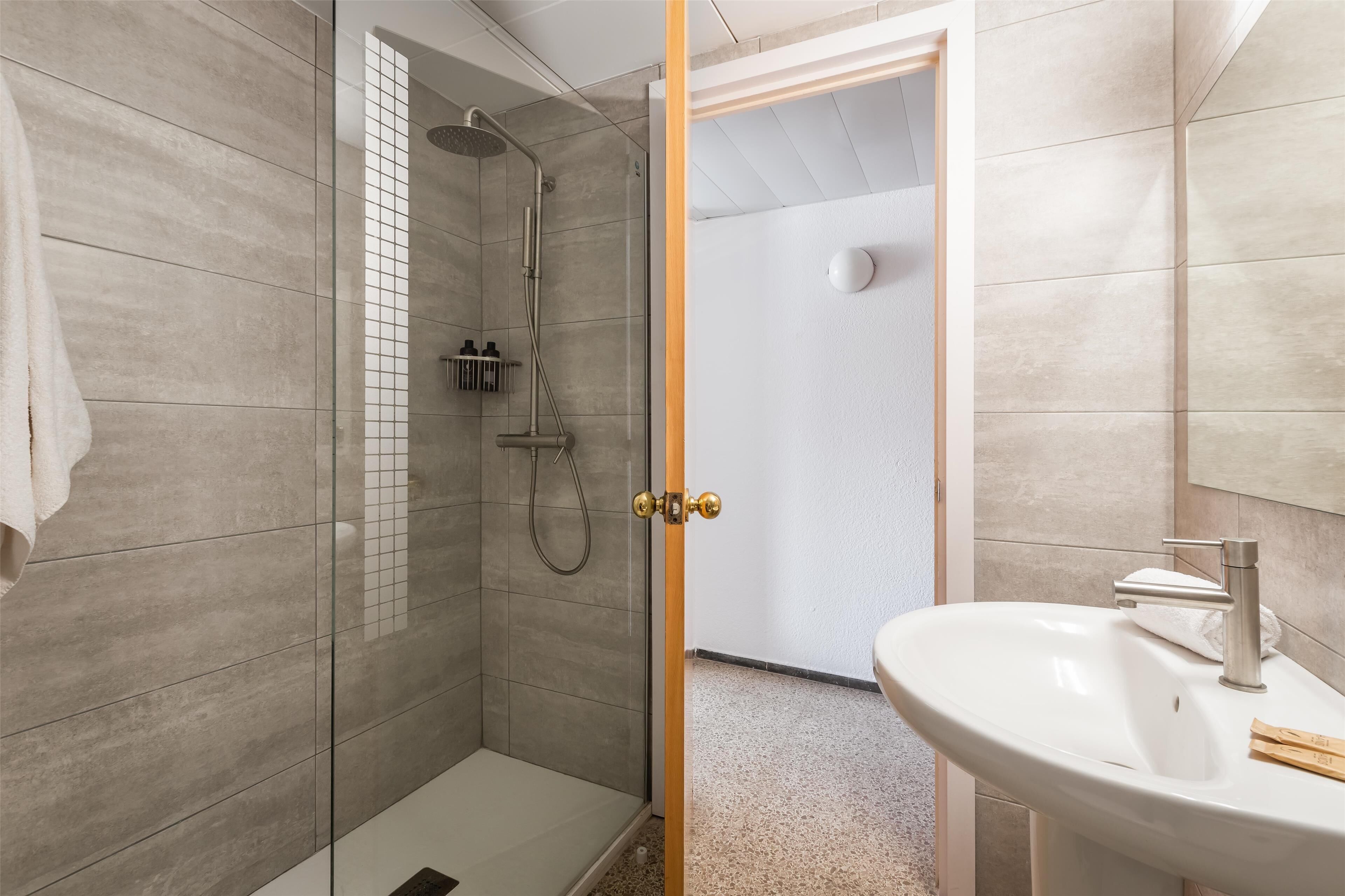 A modern bathroom with a glass-enclosed shower, a white sink, and a wooden door.
