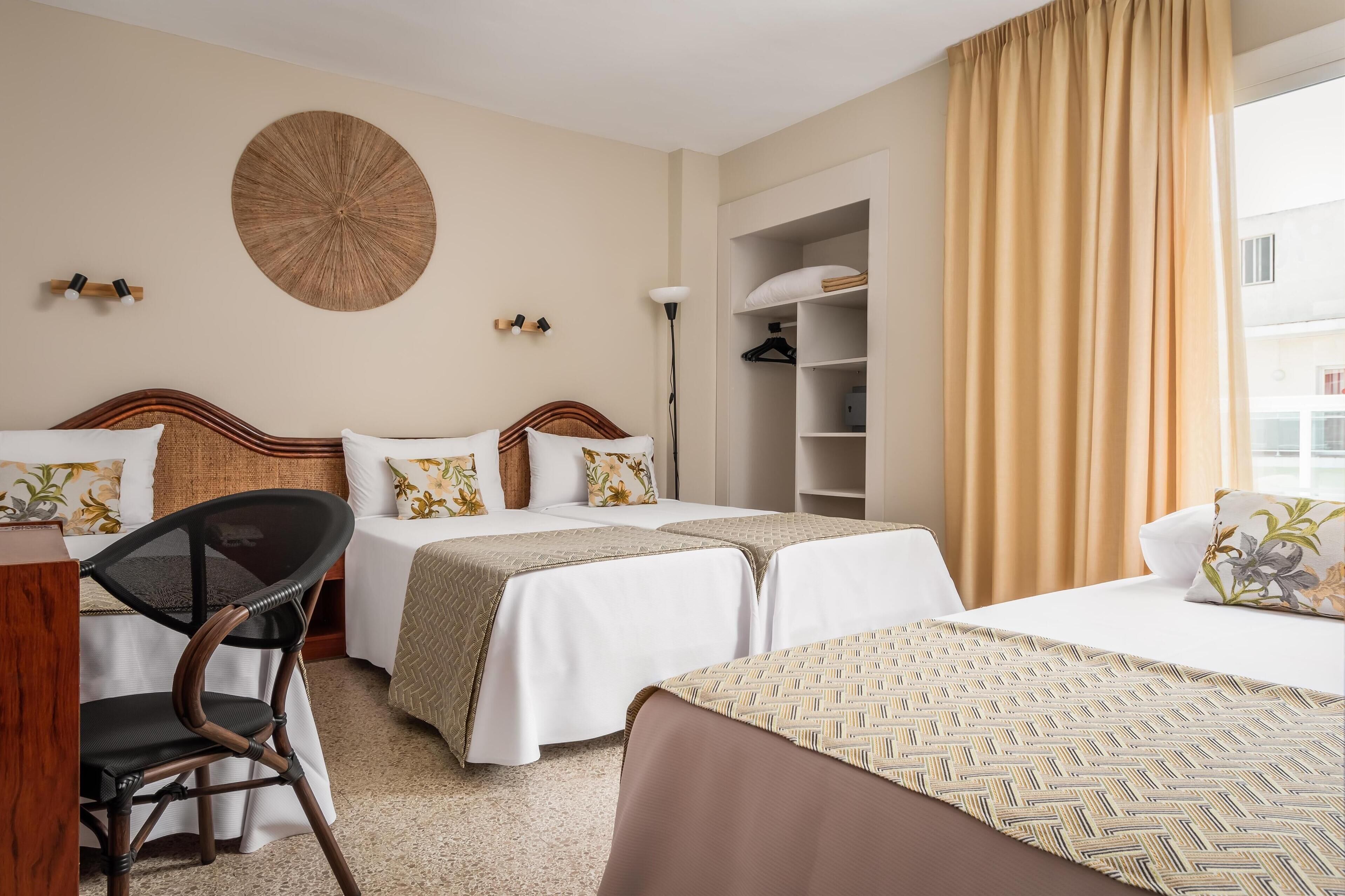 Une chambre d’hôtel avec deux lits, une chaise, une armoire et une grande fenêtre avec des rideaux.