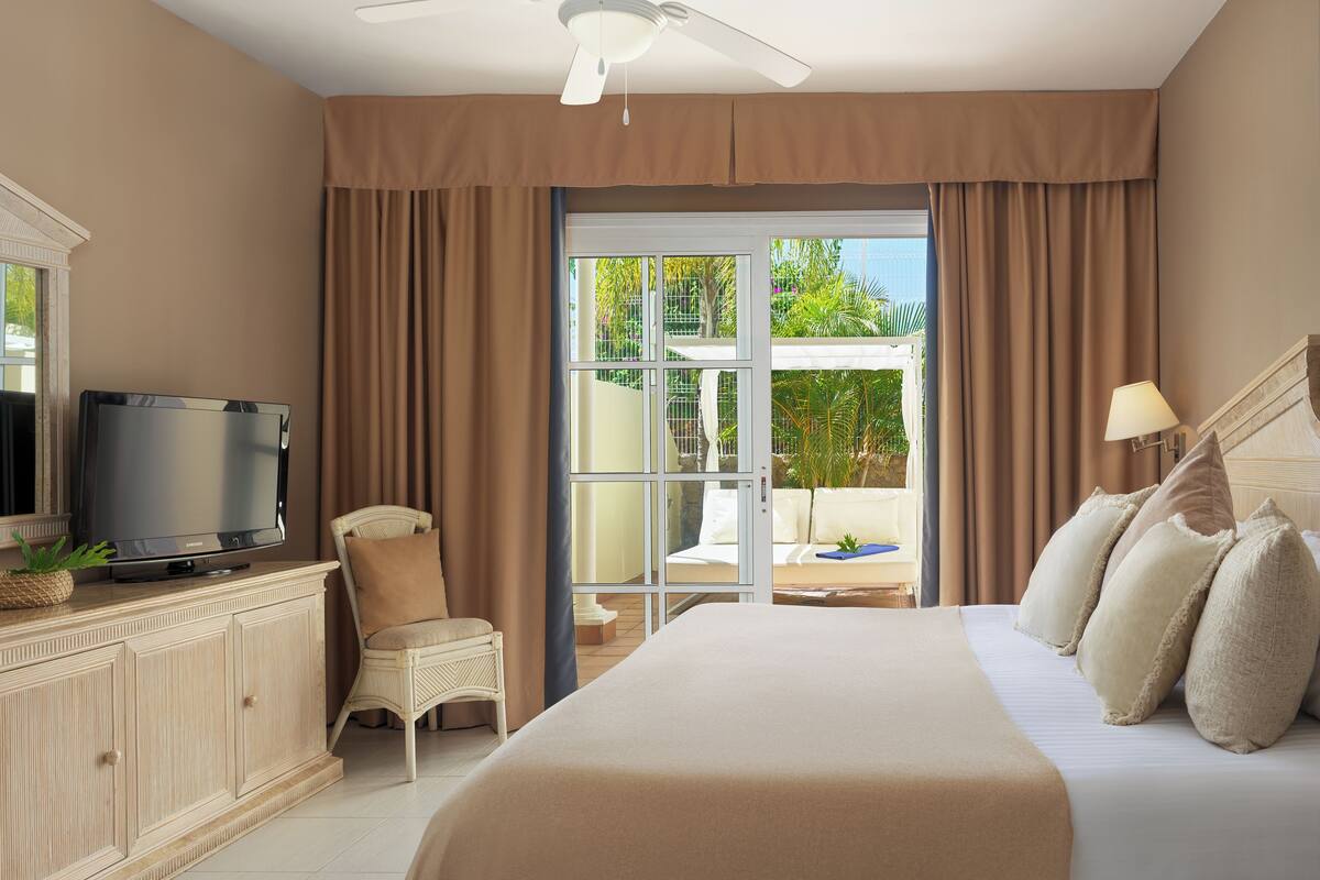 A hotel room with a bed, a television, a chair, and a view of the outdoors.