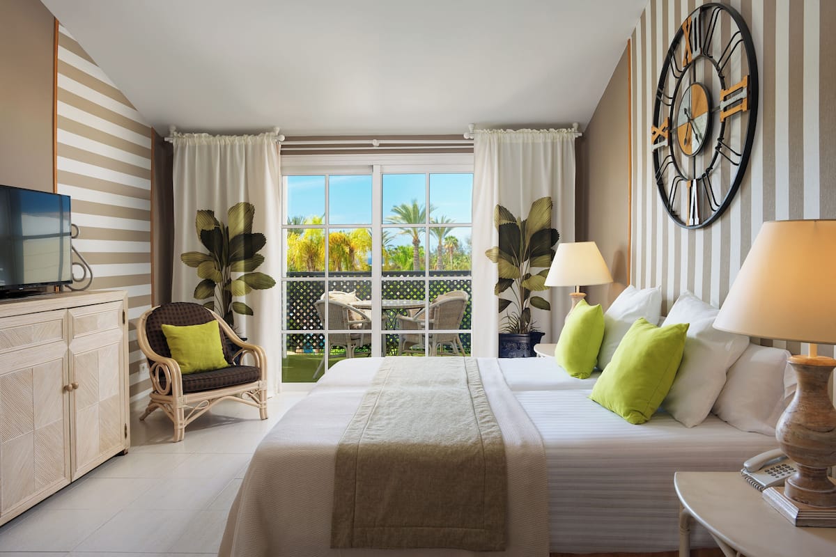 A hotel room with a bed, a TV, a desk with a lamp, and a view of the outdoors.