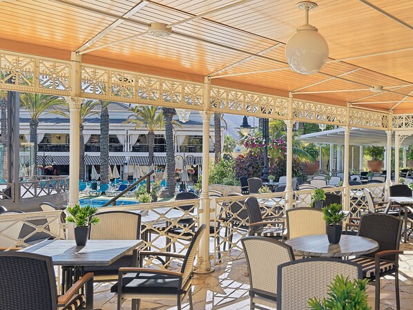 An outdoor patio with tables and chairs, overlooking a pool and a building with balconies. - Gran Oasis Resort (Arona)