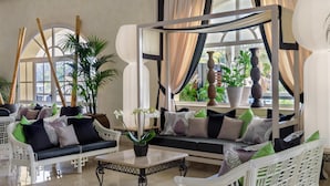 Un vaste espace salon aménagé avec des meubles en osier, une table basse centrale et des plantes en pot.