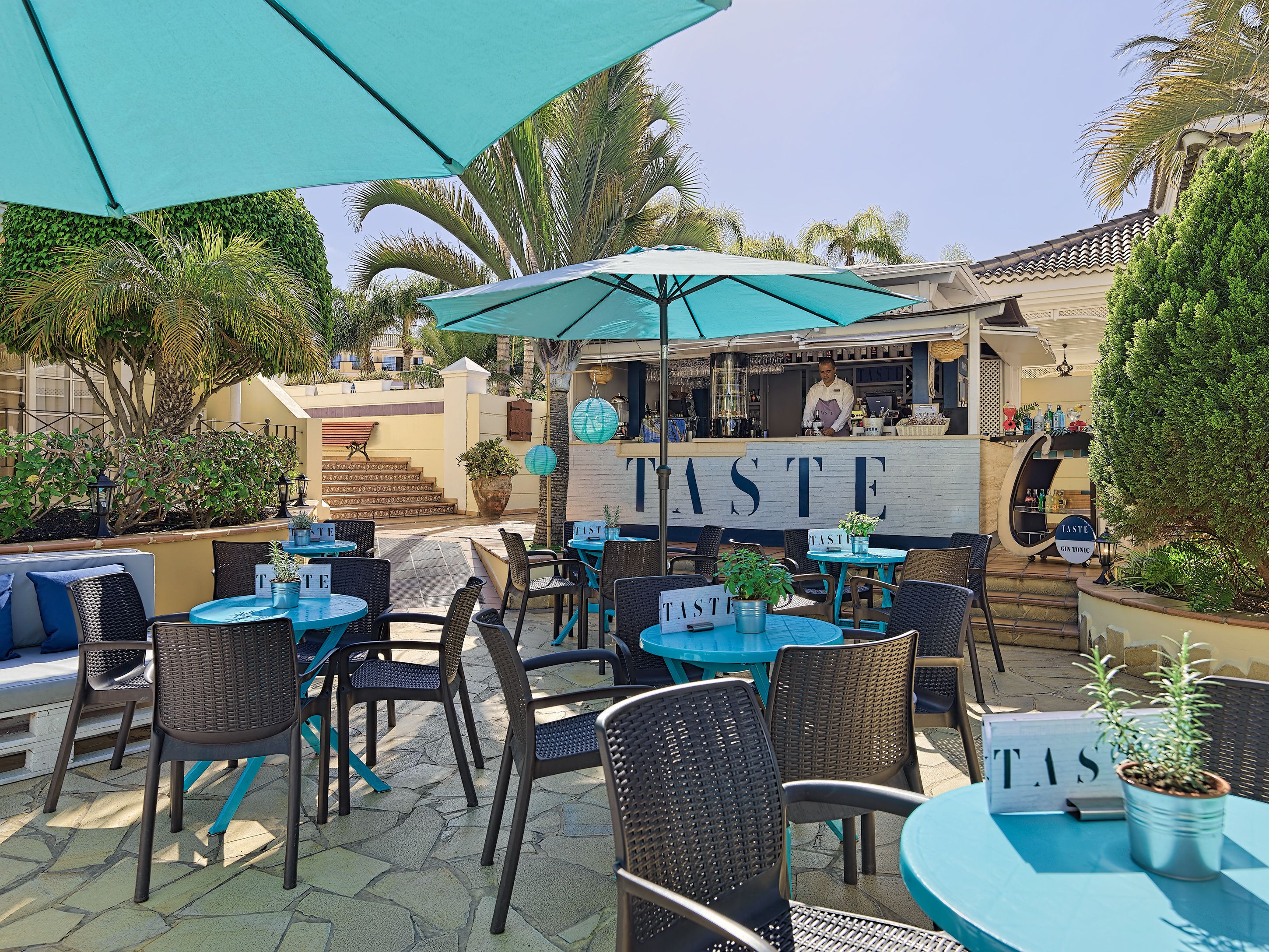An outdoor seating area with tables and chairs, a bar area, and a sign that reads "TASTE".