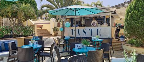 An outdoor seating area with tables and chairs, a bar area, and a sign that reads "TASTE".