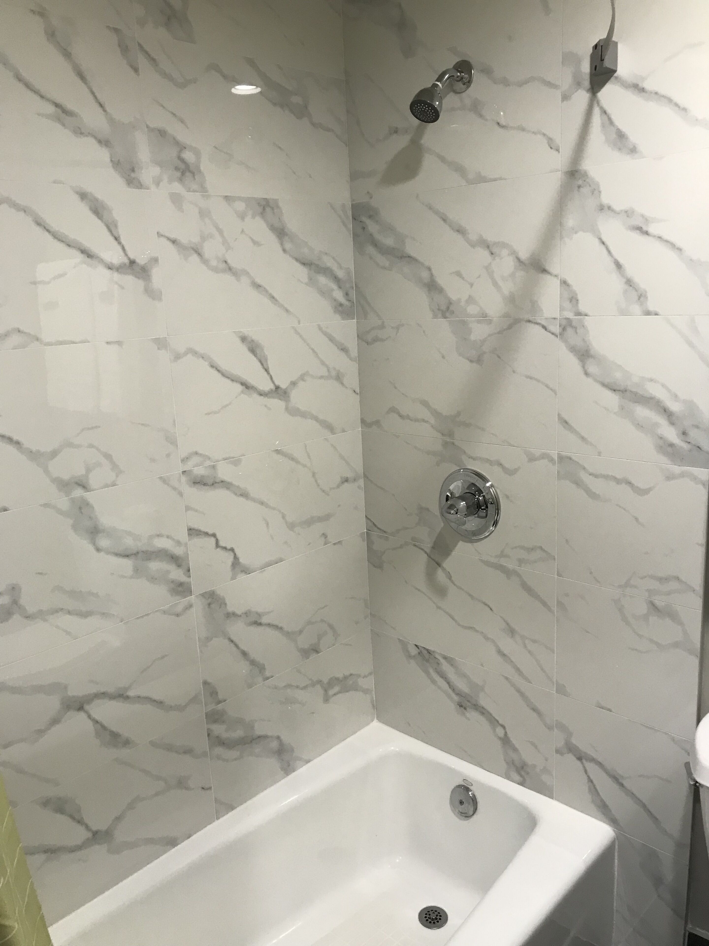 A bathroom with a white bathtub, a shower with a handheld showerhead, and a wall-mounted faucet.