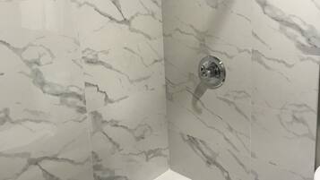 A bathroom with a white bathtub, a shower with a handheld showerhead, and a wall-mounted faucet.