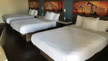 Habitación de hotel con tres camas, cada una con ropa blanca y cabeceros de madera. En las paredes, cuadros de plataformas petrolíferas.