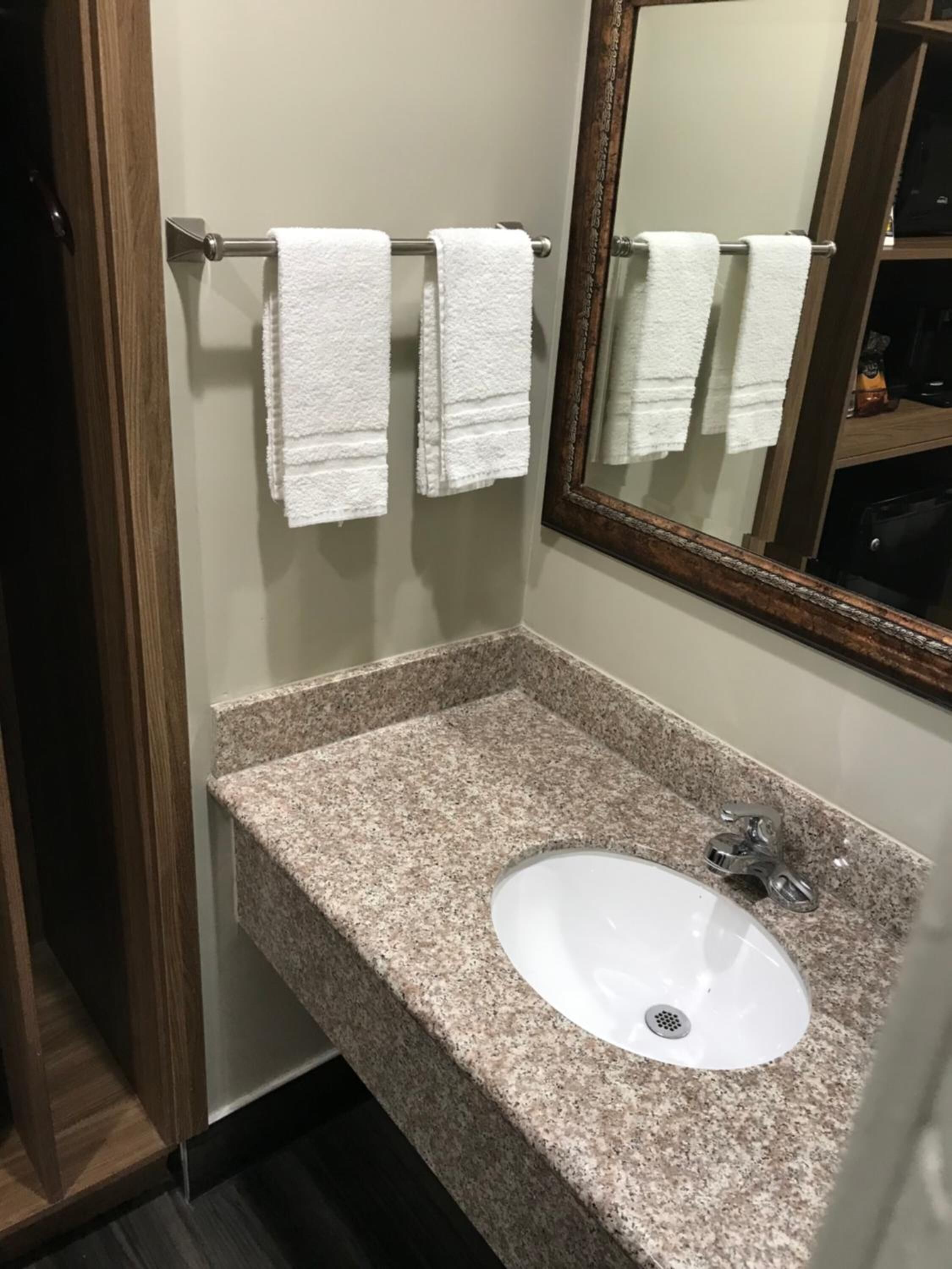 Un baño con lavamanos de encimera de granito, un espejo y dos toallas blancas colgadas en un perchero metálico.