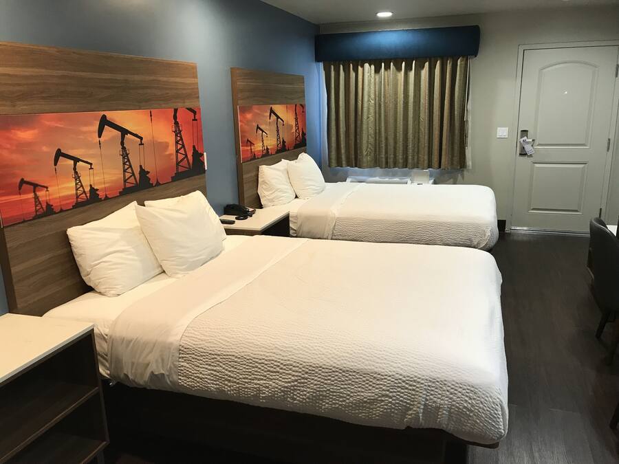 A hotel room with two beds, a nightstand, a desk, and a painting of oil pumps.