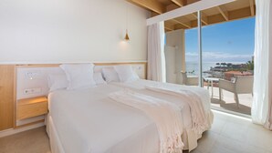 A bedroom with a large bed, a bedside table, a nightstand, a wall socket, and a view of the ocean through a sliding glass door. - Iberostar Selection Anthelia (Adeje)