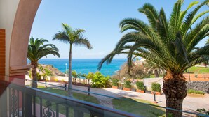 A balcony with a view of the sea, palm trees, and a stone wall. - Iberostar Selection Anthelia (Adeje)