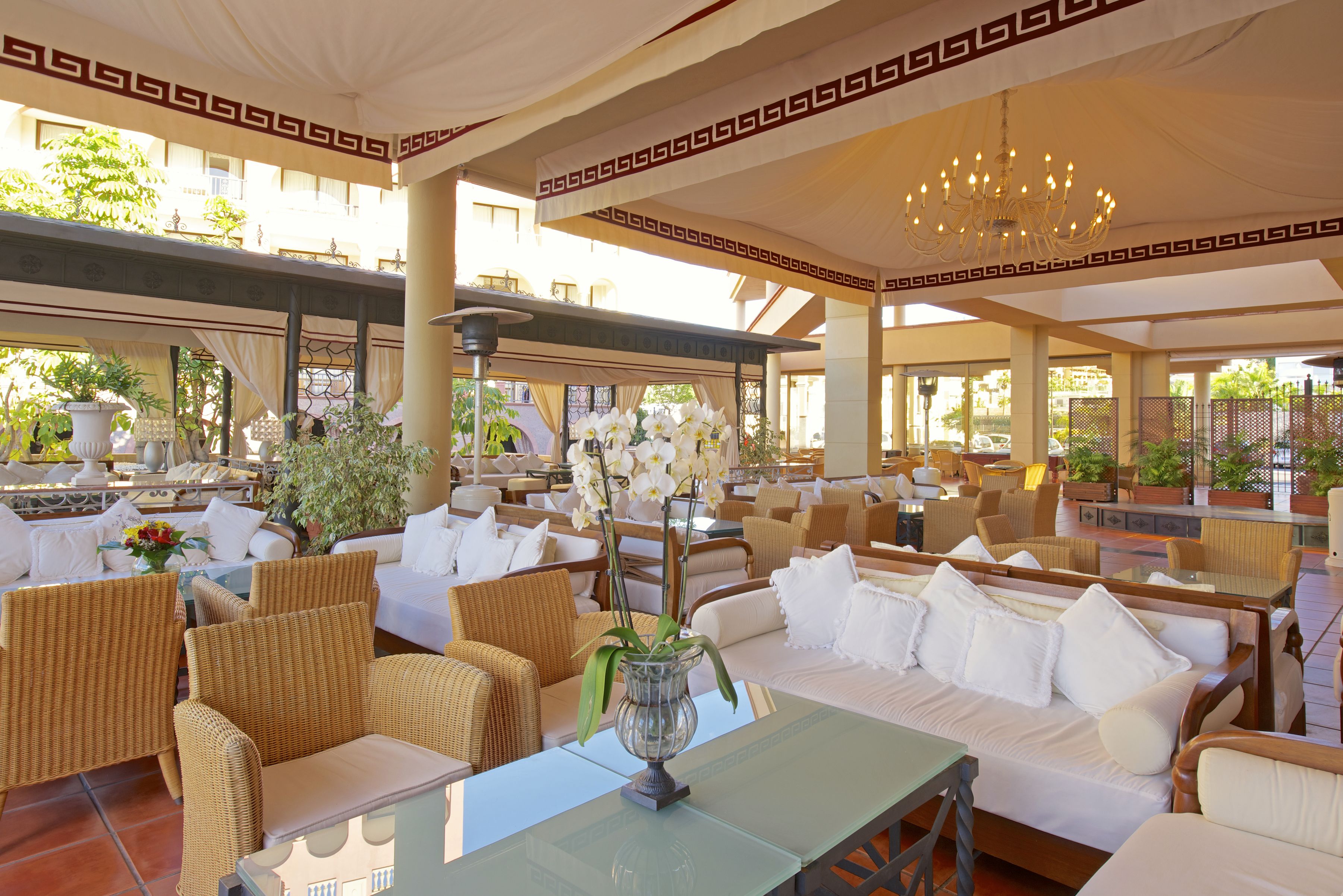 A spacious outdoor seating area with wicker furniture, white cushions, and a glass table with a vase of flowers.