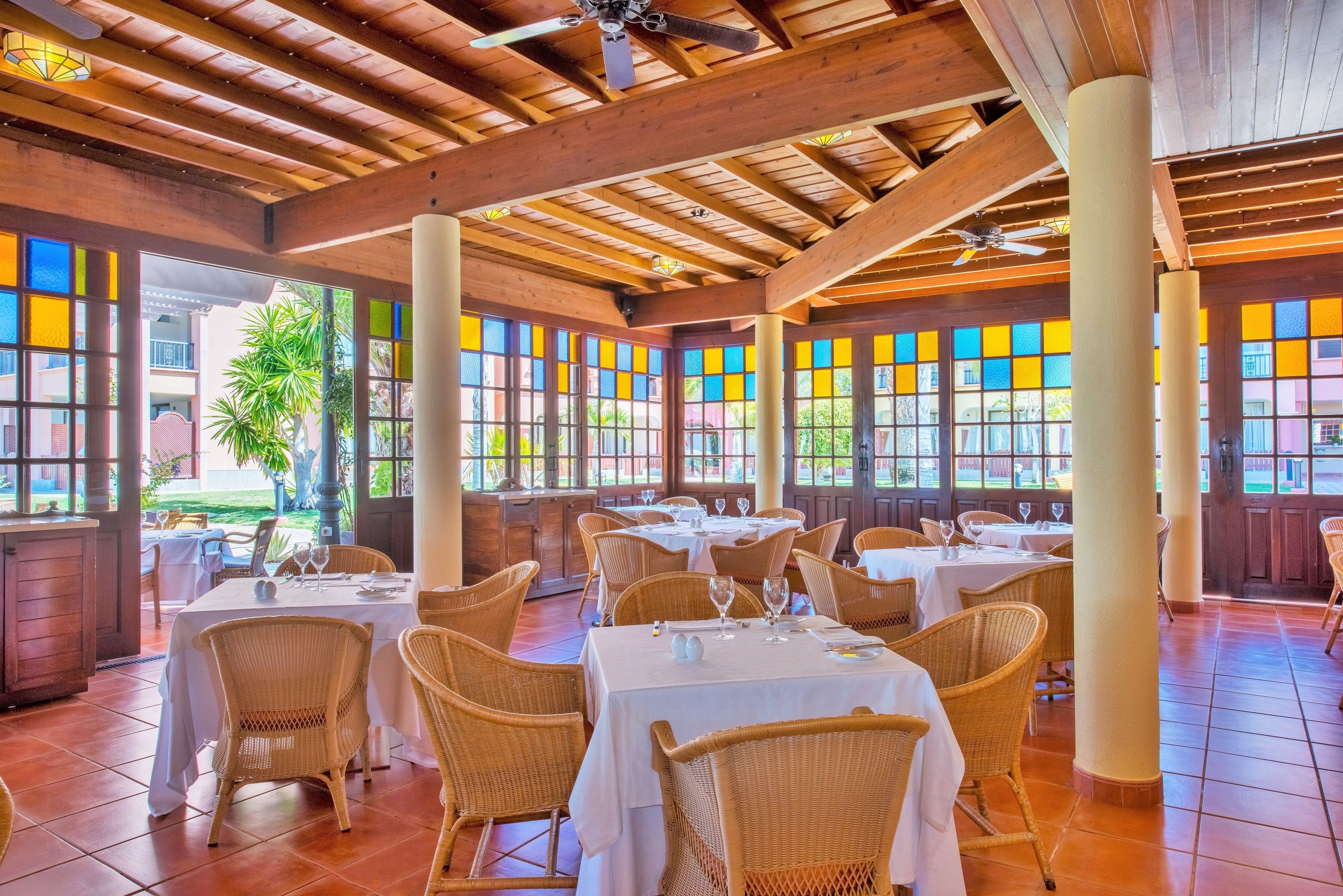 Un restaurante con vigas de madera, sillas de mimbre y mesas dispuestas para comer.