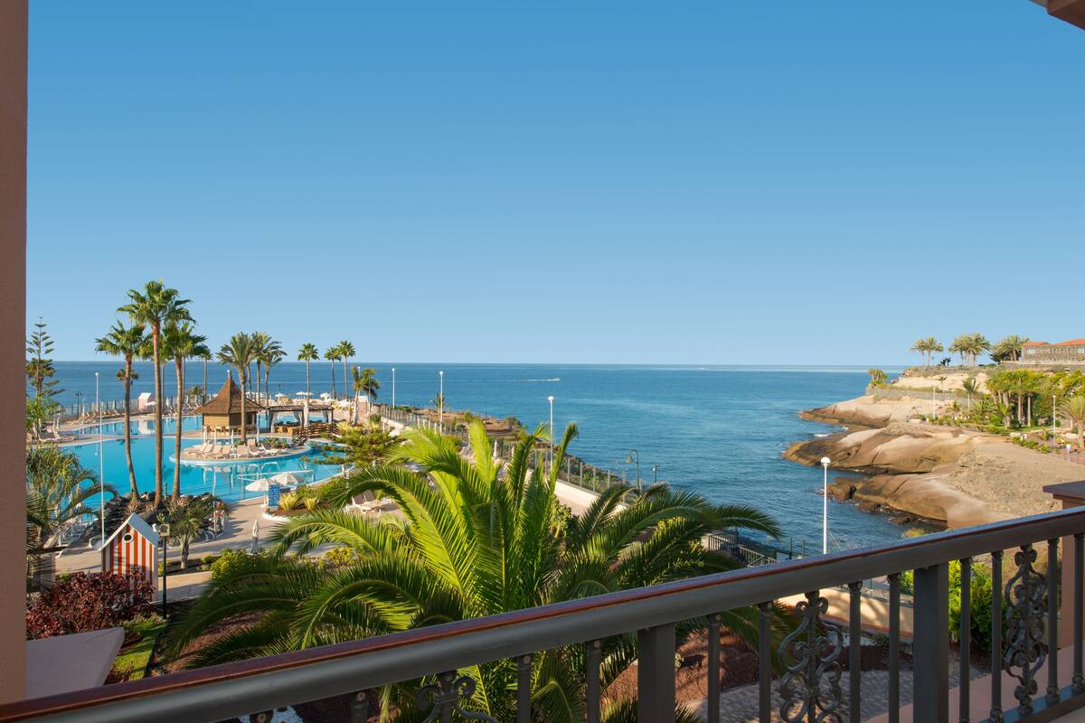 Um resort com piscina, palmeiras e vista para o oceano.