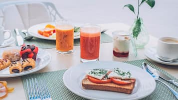 Un desayuno con tostadas, un vaso de zumo de naranja, un vaso de zumo rojo, una taza de café y un pequeño florero con una planta.