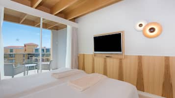 Een hotelkamer met twee bedden, een televisie en een balkon met uitzicht op gebouwen.