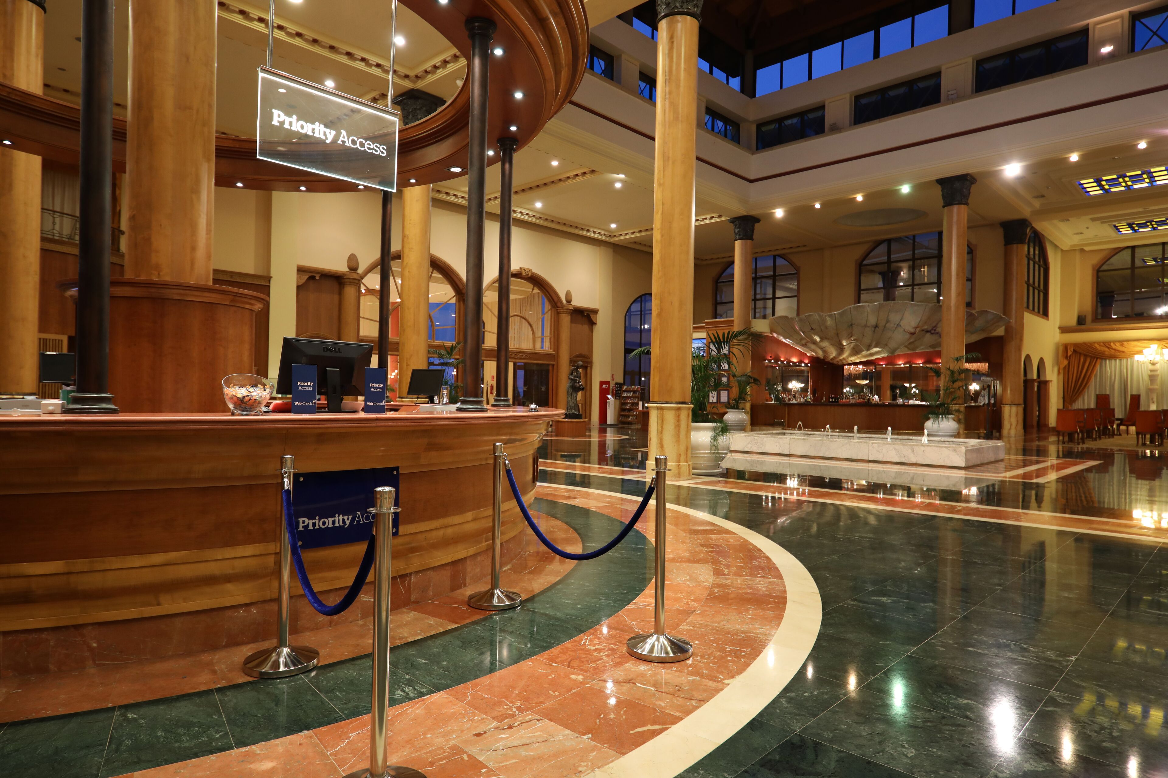 A spacious lobby with a marble floor, a reception desk, and a 'Priority Access' sign.