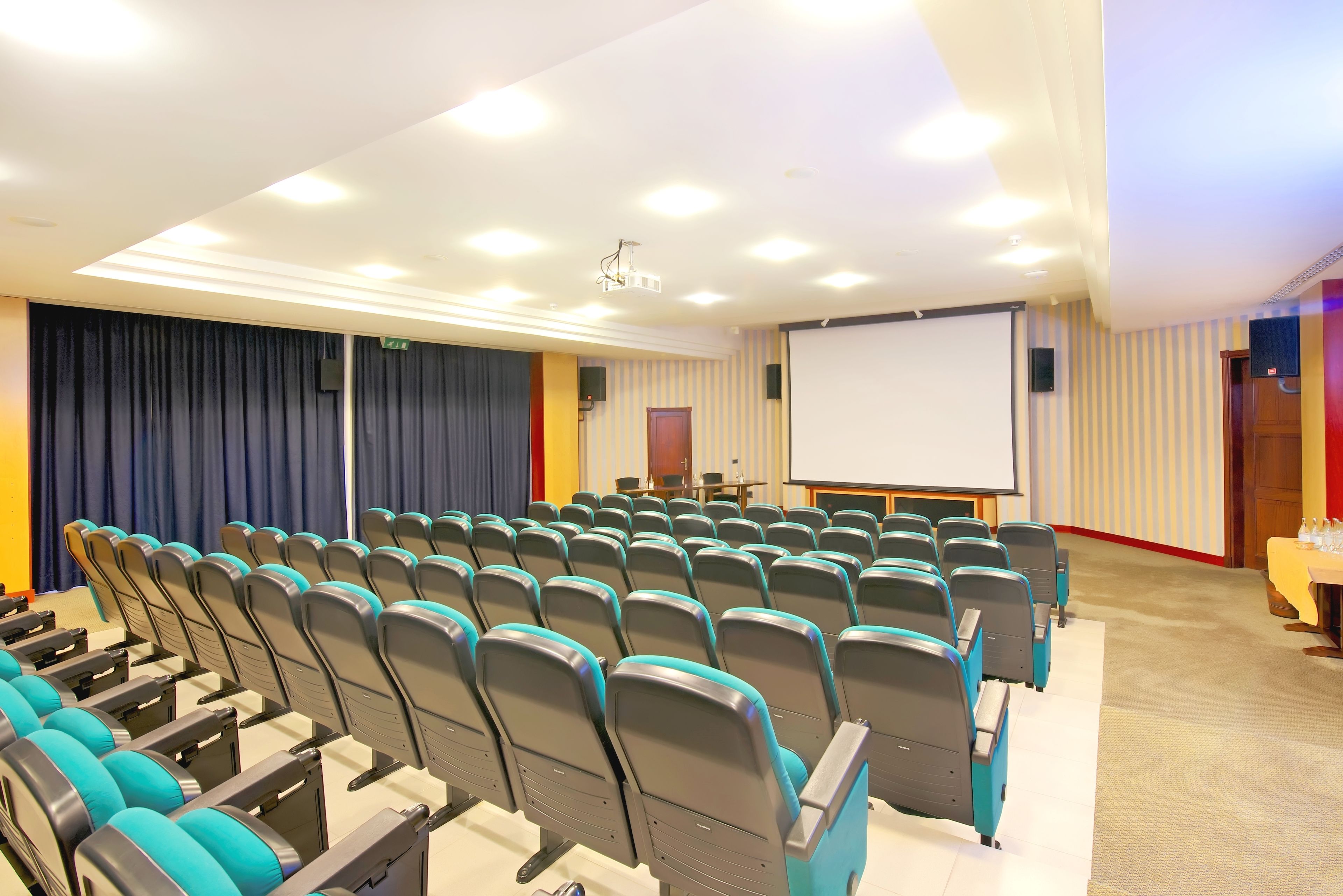 Une salle de conférence avec des rangées de chaises, un écran de projection et un tableau blanc.