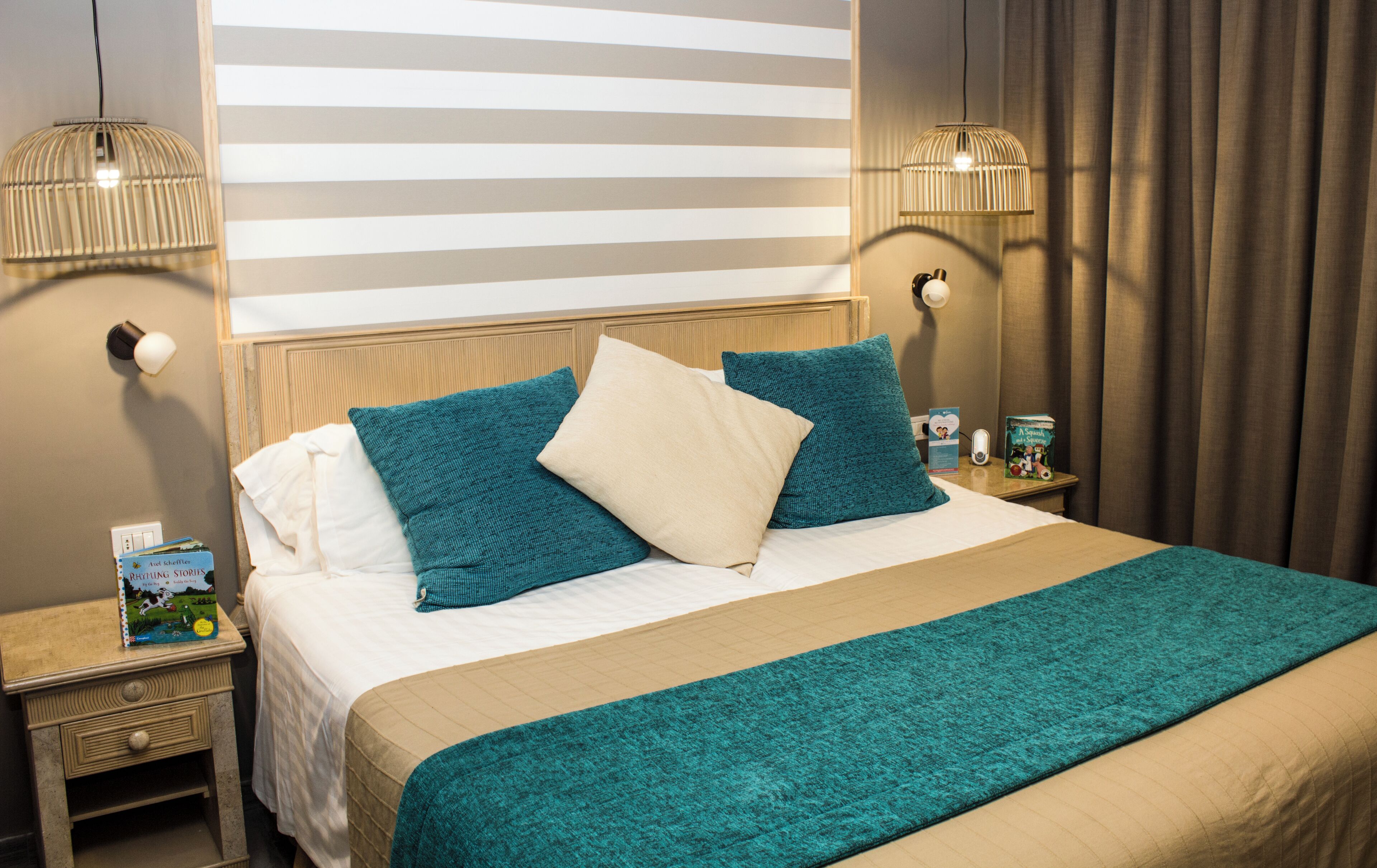 A neatly made bed with a teal and beige bedspread, two pillows, and a bedside table with a book and a lamp.