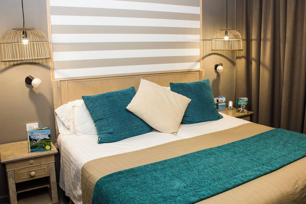 A neatly made bed with a teal and beige bedspread, two pillows, and a bedside table with a book and a lamp.