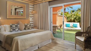 A hotel room with a large bed, a ceiling fan, a balcony with wicker furniture, and a view of palm trees. - GREEN GARDEN ECO RESORT & VILLAS (Arona)