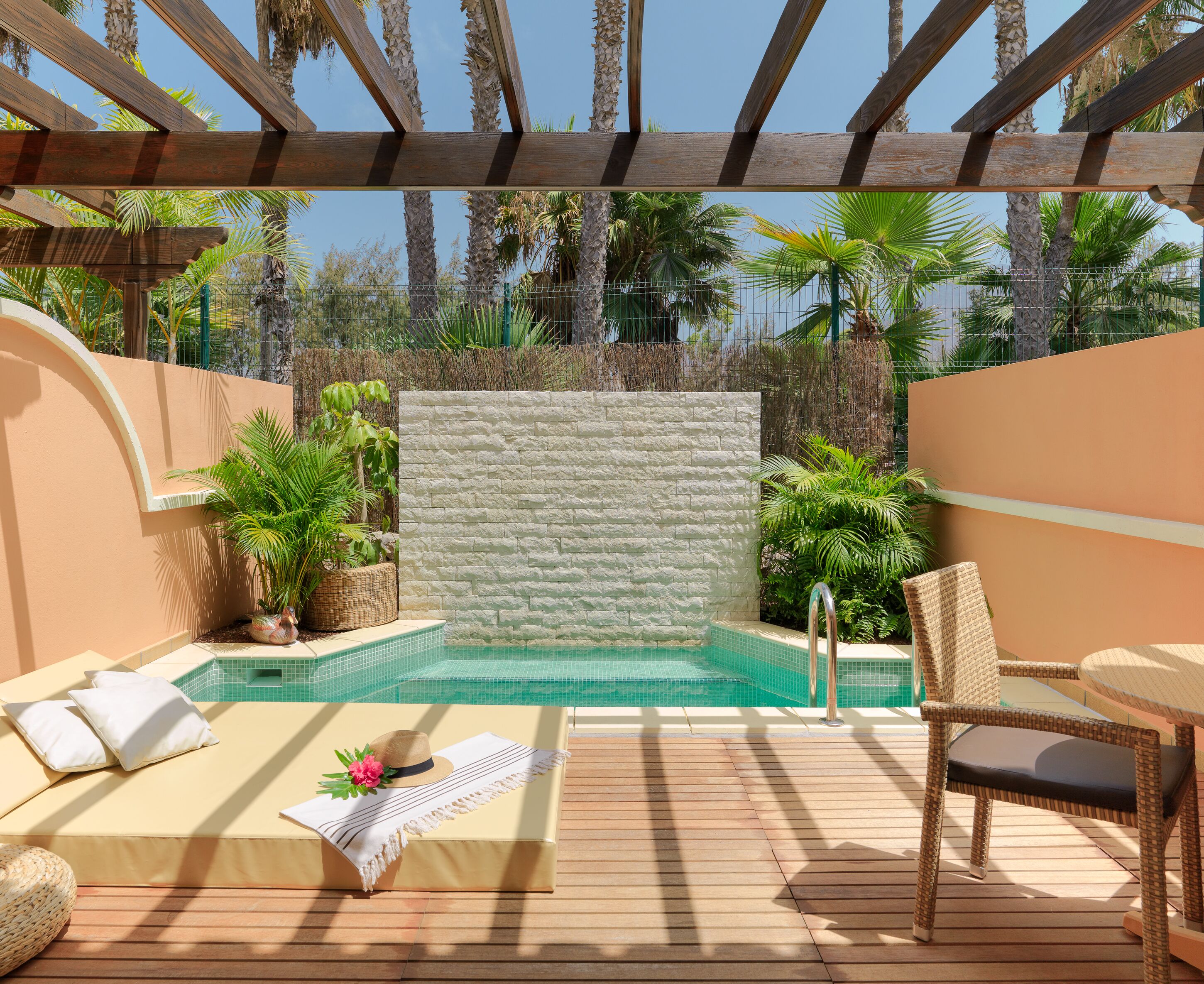 Un espace piscine doté d’une terrasse en bois, de chaises longues, d’un petit jacuzzi et d’un mur en pierre servant de décor.