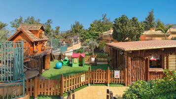 A wooden play area with a fenced entrance, a small green playhouse, and a large blue ball.
