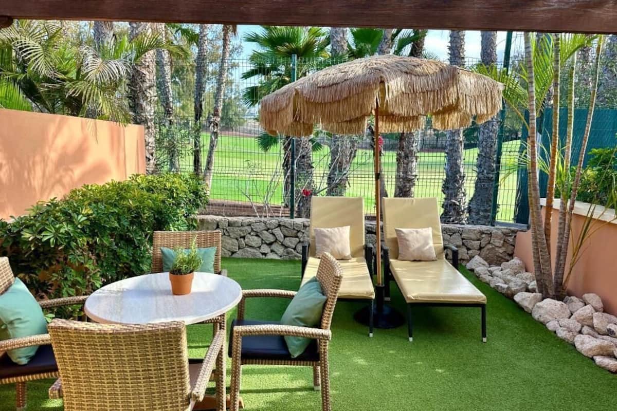 Eine Terrasse im Freien mit Korbmöbeln, einem runden Tisch und einem Reedschirm.