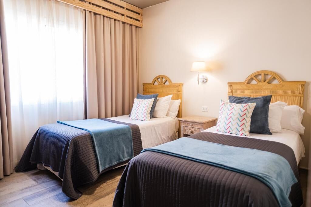 Et hotelværelse med to senge, hver med en træsenggavl, et sengebord og en lampe.