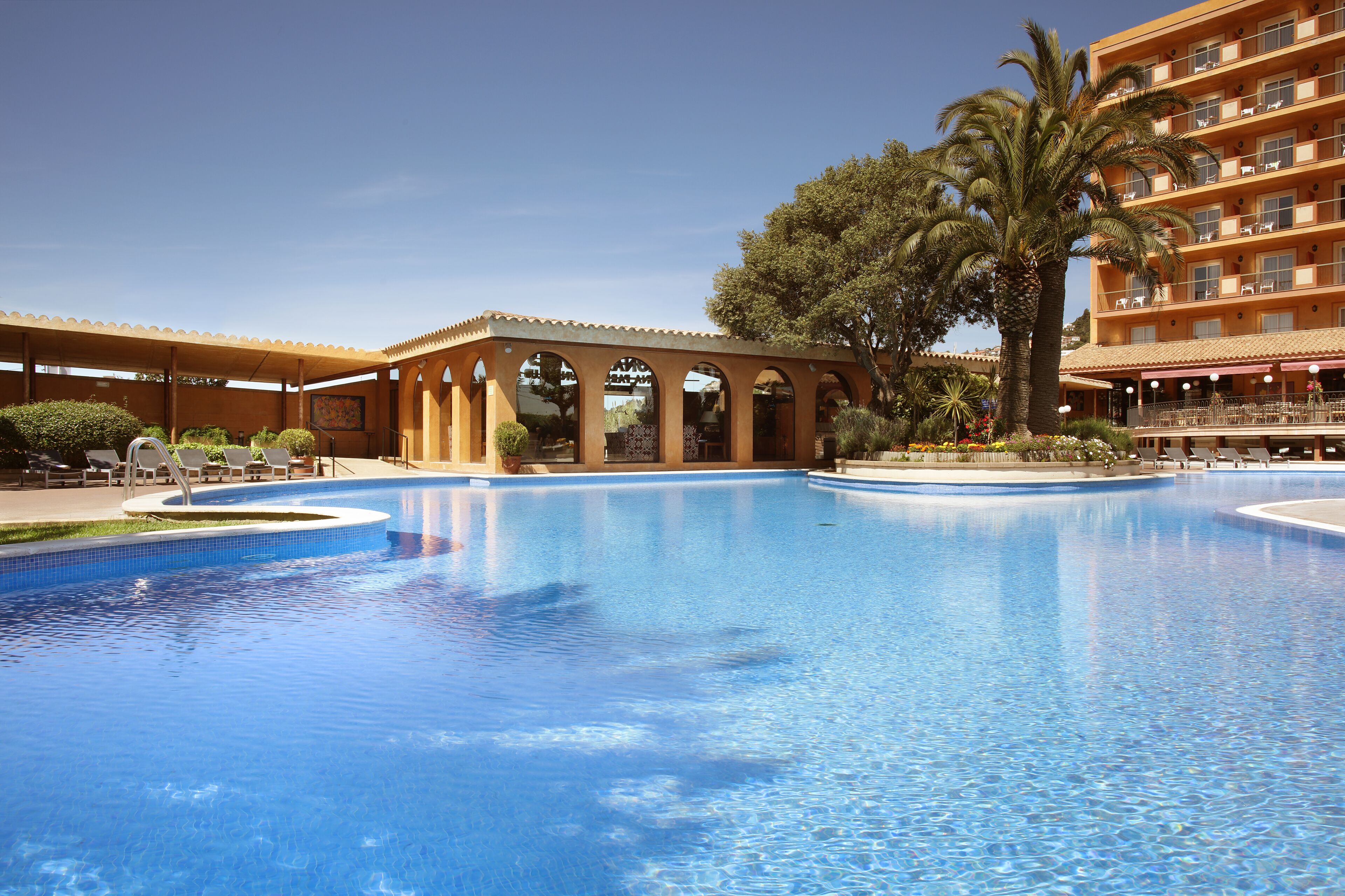 Ett hotell med en stor swimmingpool, en överbyggd paviljong och en palmpalm.