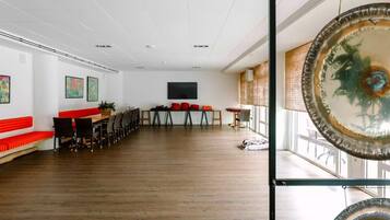 A spacious room with a long wooden table, red benches, and a large window.