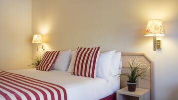 A neatly made bed with striped bedding, two bedside lamps, and a potted plant on the nightstand.
