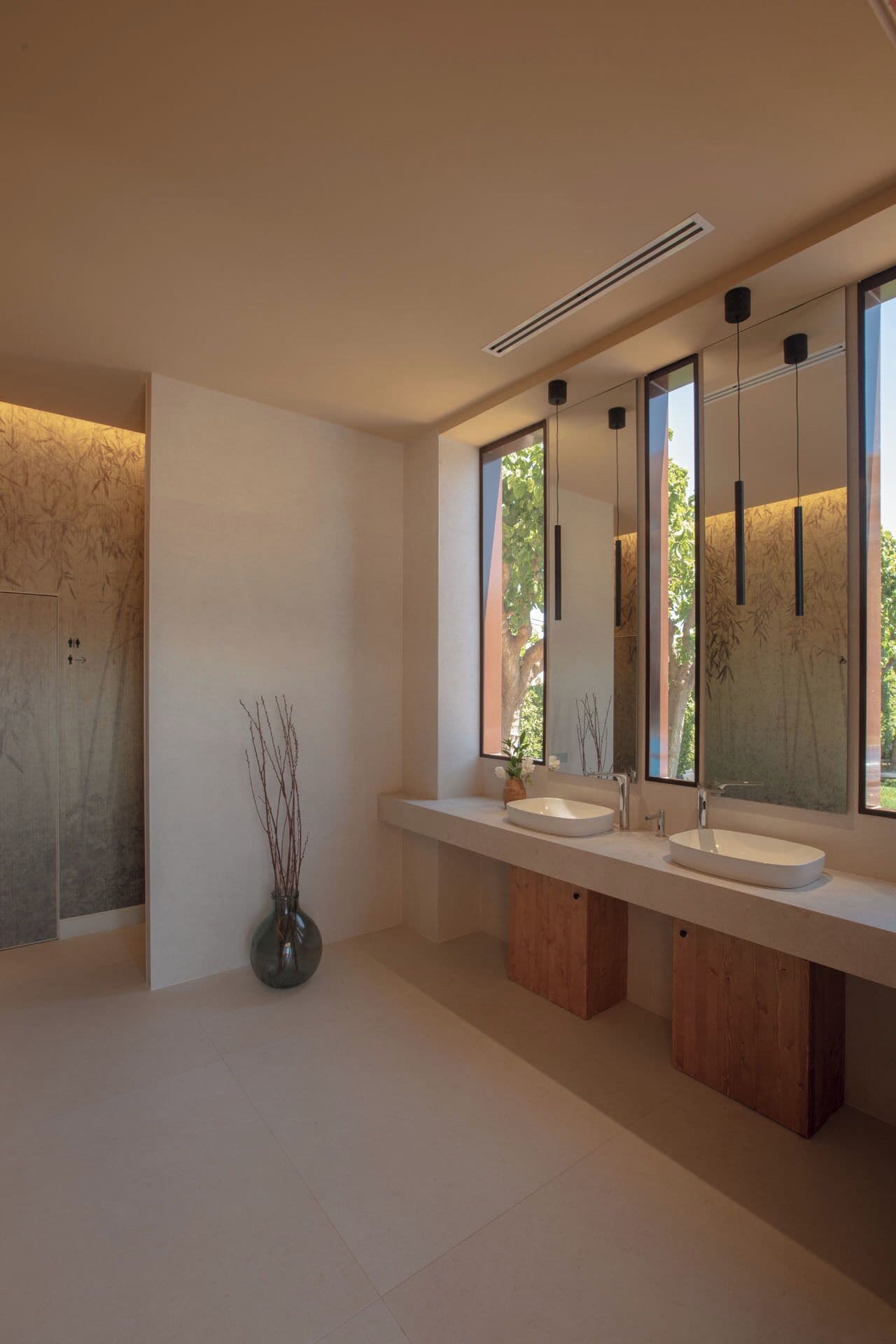 Een moderne badkamer met twee wastafels, een grote spiegel en een vaas met takken.
