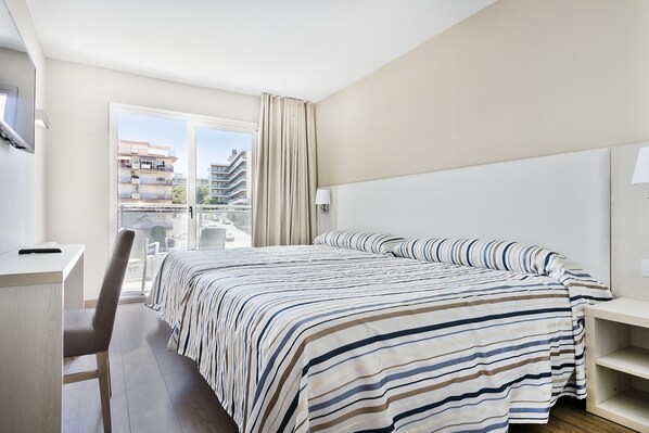 Habitació d'hotel amb llit, escriptori, cadira i finestra amb cortines.