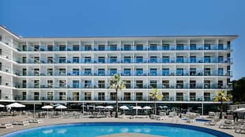 Un hotel de diversos pisos amb piscina, seients a l'aire lliure i palmeres.