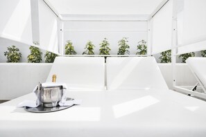Una habitación moderna y minimalista con una mesa blanca, una botella de champán y copas, rodeada de plantas en macetas.