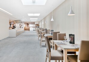 Un restaurant modern amb una barra llarga, diverses taules i il·luminació penjant.