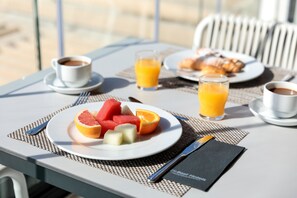 Taula de petit esmorzar amb un plat de fruita, dues flaites de suc d'aranja i una tassa de cafè.