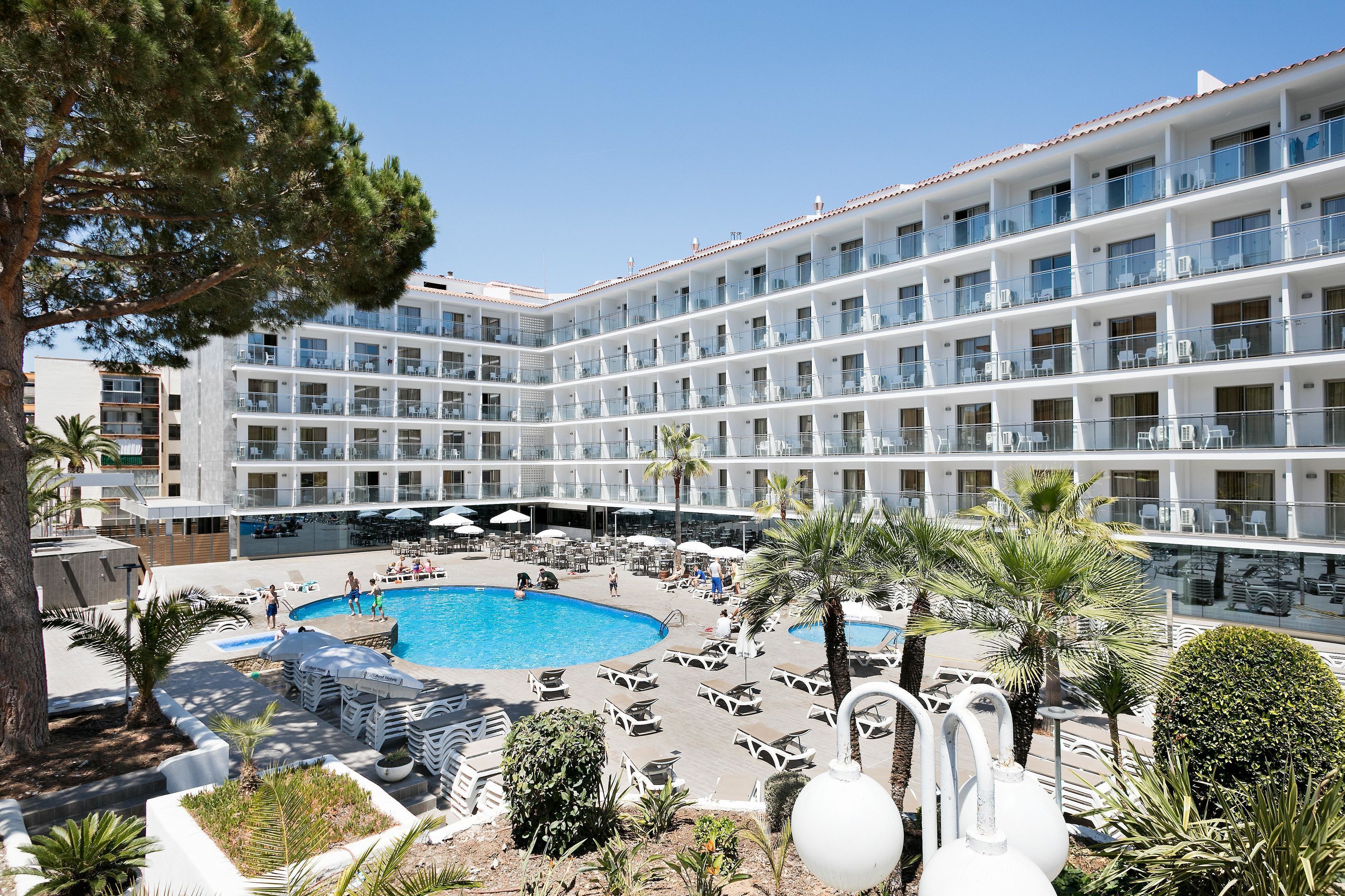 Un hotel amb nombroses balcons, una piscina i gandules.