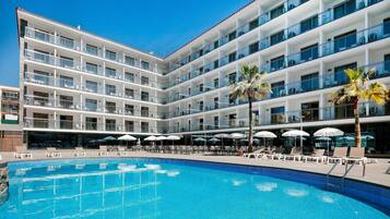 Un hotel de diverses plantes amb piscina, mobiliari exterior i palmeres.