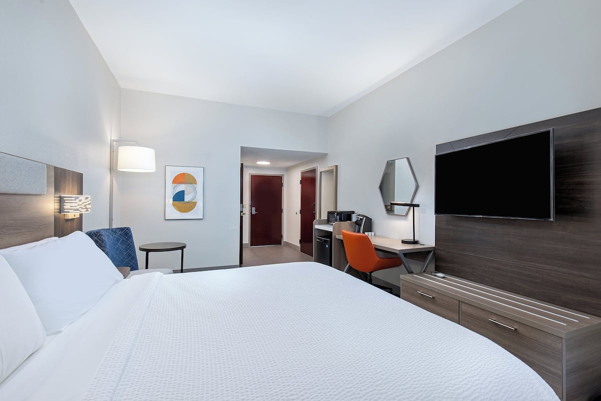 Une chambre d’hôtel moderne, dotée d’un grand lit, d’un bureau, d’une chaise, d’une télévision et d’une salle de bain visible à travers une porte ouverte.