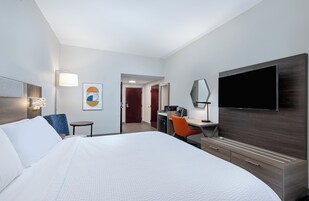 Una habitación de hotel con una cama grande, un escritorio con una silla, un televisor de pantalla plana y un baño visible a través de una puerta abierta.