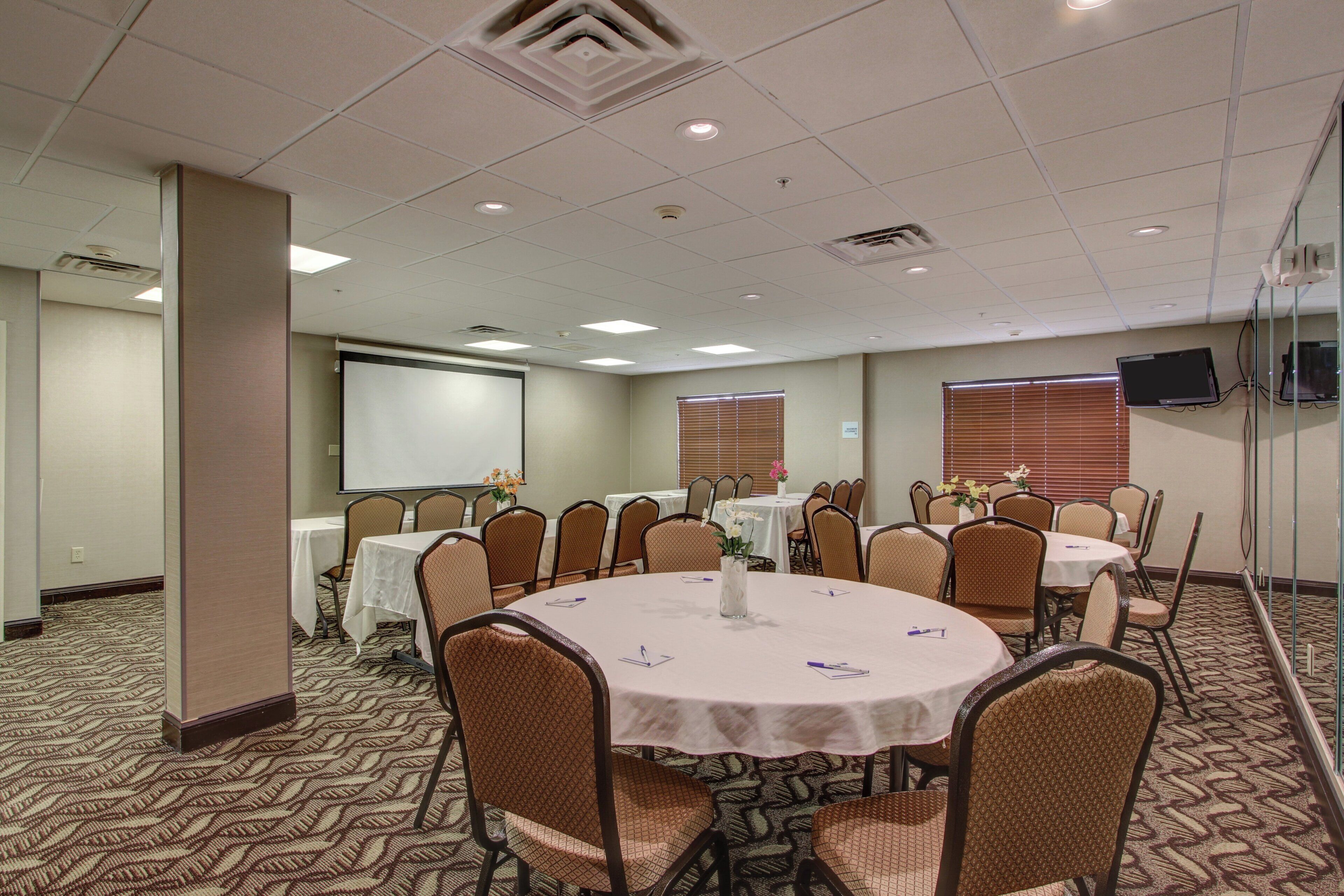 A conference room with round tables, chairs, a projector screen, and a carpeted floor.