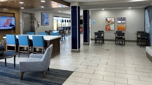 Eine moderne Hotelhalle mit Sitzgelegenheit, einer Rezeption und einem Fernseher, der Wetterinformationen zeigt.